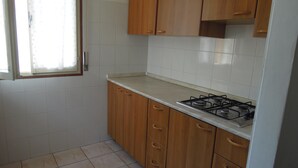 A kitchen with white tiles, wooden cabinets, a gas stove, and a window with a curtain.