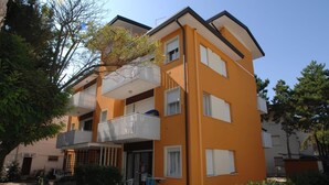 A multi-story residential building with balconies, a small outdoor seating area, and a clear sky.