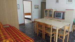 A room with a bed, a dining table with chairs, a television, and a cabinet.