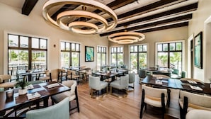 A spacious dining area with multiple tables and chairs, large windows offering views of greenery, and a modern ceiling design. - Last Minute Disney Getaway! Private Pool, Hot Tub & Games Room. Book Now! #16468 (Orlando)