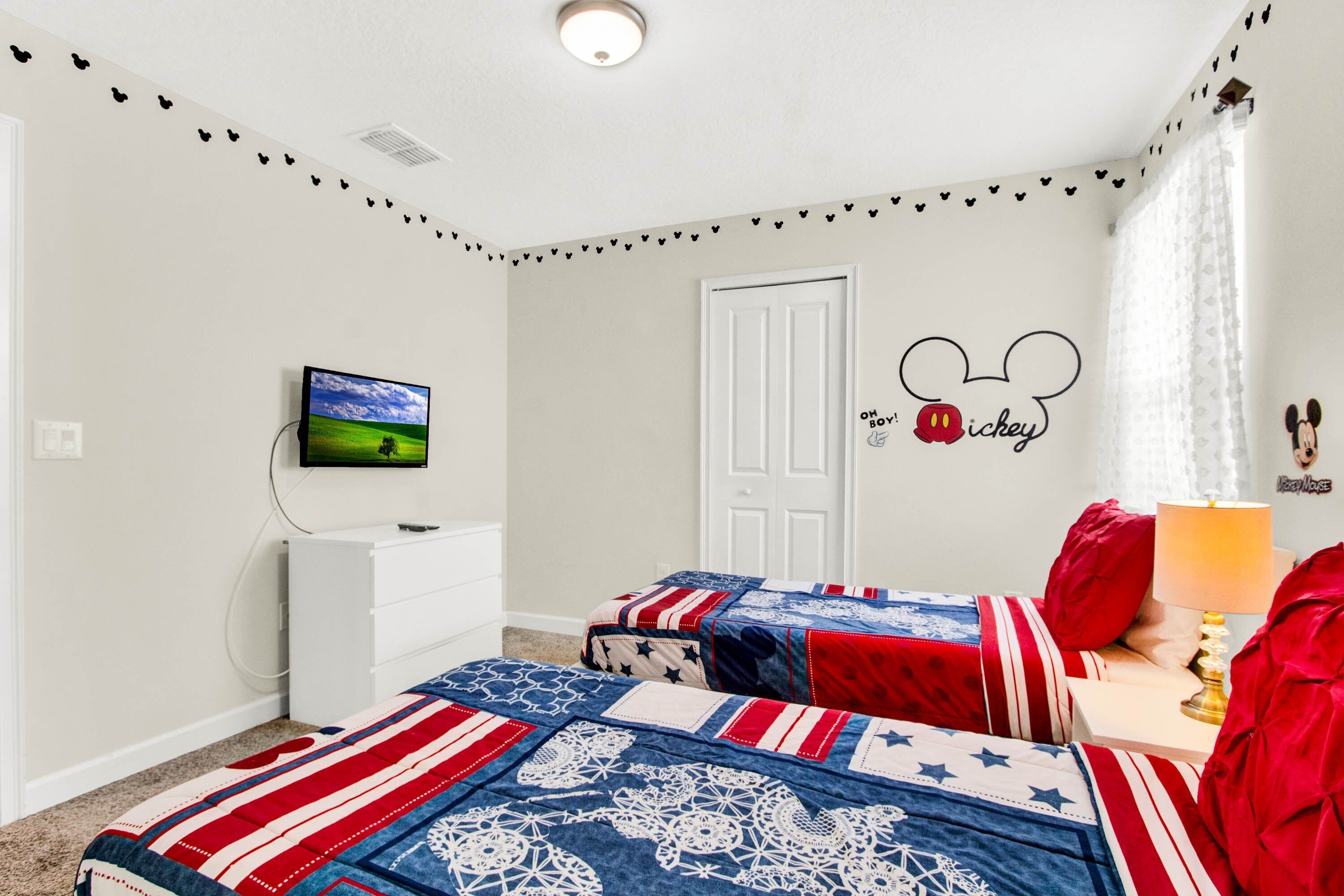 A bedroom with two beds, a TV, a dresser, and Mickey Mouse wall decal.