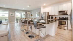 Une cuisine moderne avec des meubles blancs, des appareils en acier inoxydable et un coin bar équipé de tabourets.