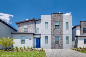 Stylish two-story residence with a contemporary design, featuring a blue door and a well-manicured lawn.