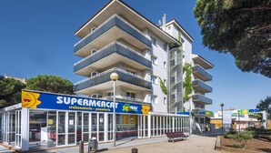 Edificio de varios pisos con un supermercado en la planta baja, destacando un frente de vidrio transparente y un letrero que dice 'Supermercat'.