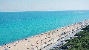 Una playa con una carretera que la bordea, bordeada de coches aparcados y sombrillas.