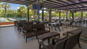 Un área de comedor al aire libre con mobiliario de mimbre y vistas a palmeras y una piscina.