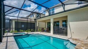 Una piscina con tetto in vetro, circondata da una zona prendisole con sedie e un piccolo giardino.