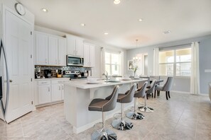 A modern kitchen with white cabinets, a central island with bar stools, and a dining area with a table and chairs.
