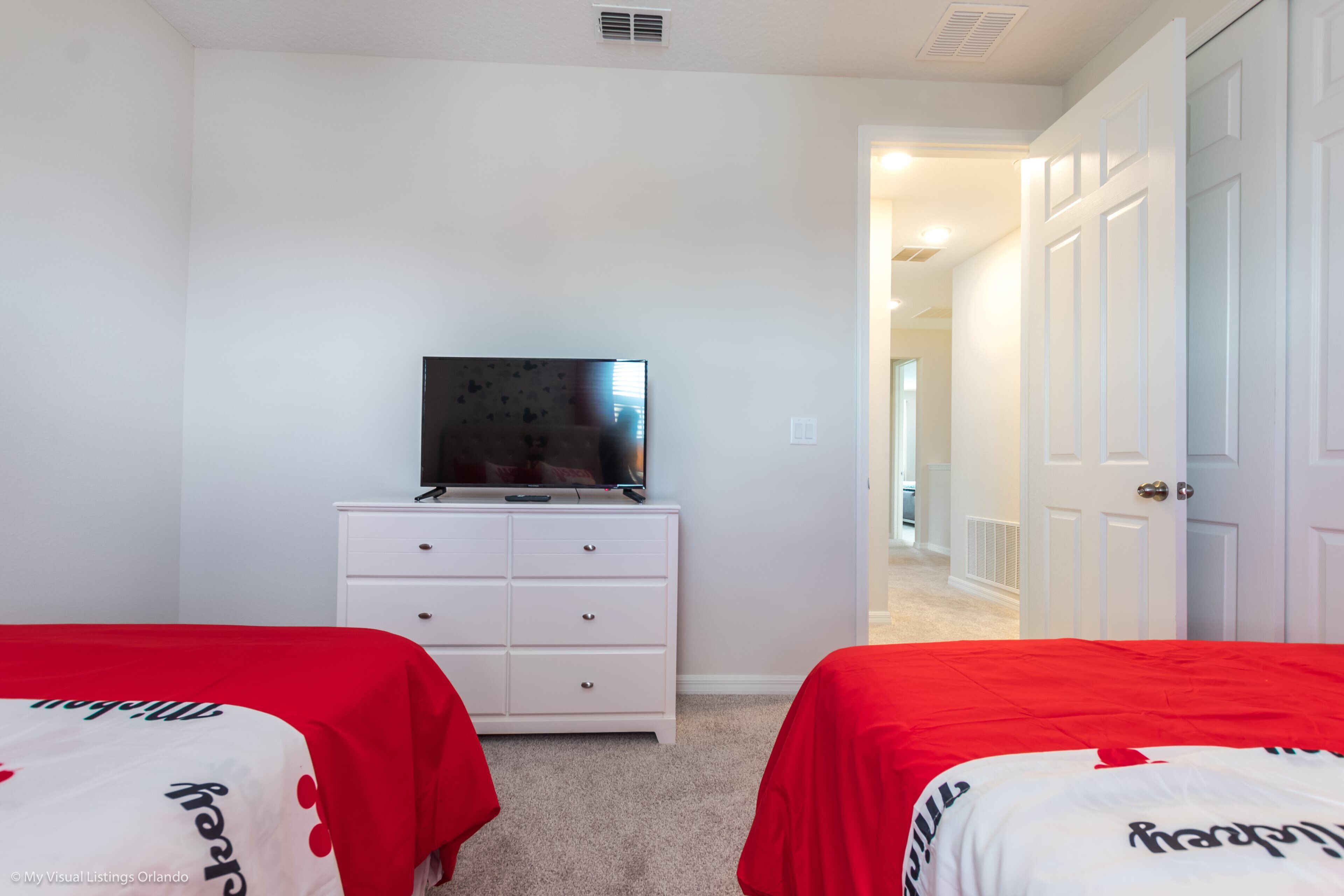 A bedroom with two beds, a TV on a dresser, and a hallway leading to another room.
