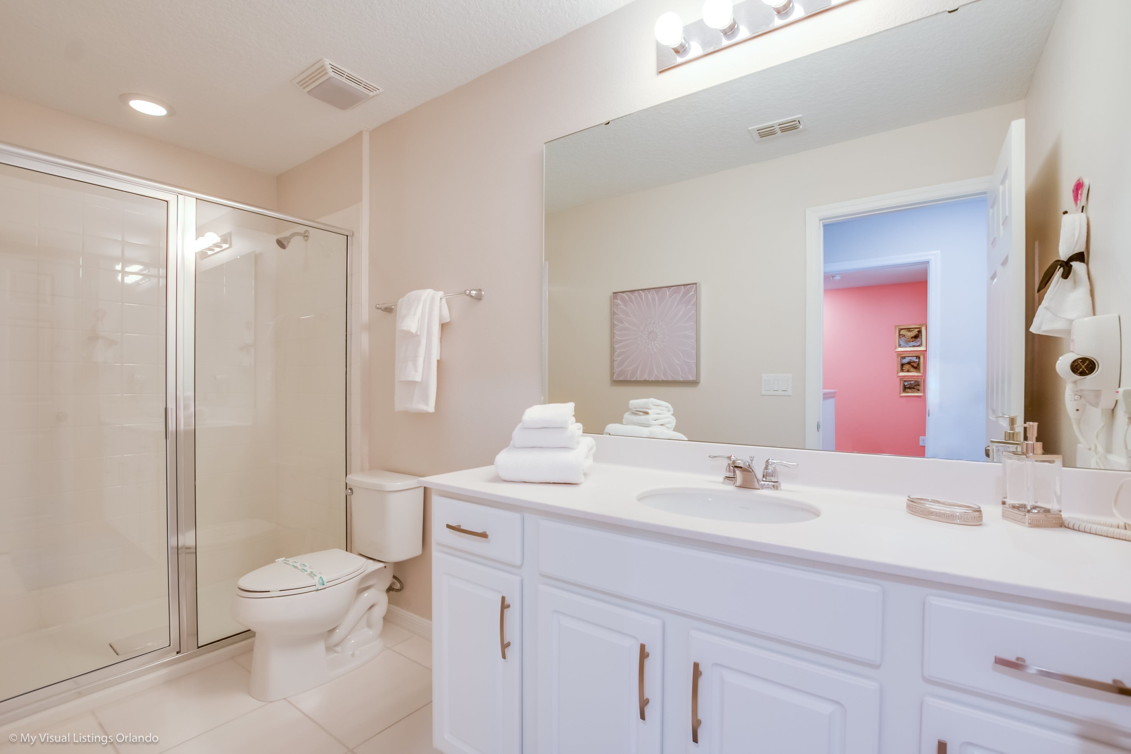 A modern bathroom with a glass shower enclosure, white fixtures, and a large mirror.