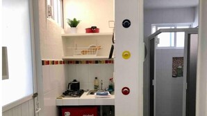 A compact kitchen with a gas stove, sink, and a red appliance, likely a refrigerator. There's a small window above the sink and a door leading to a bathroom. - Apartaestudio#4 Itesm Pequeño, Acogedor & Céntrico (Santiago de Querétaro)