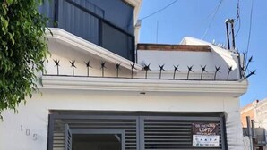 A building with a closed metal shutter door, a sign indicating it is for rental, and a number '105' on the wall. - Apartaestudio#4 Itesm Pequeño, Acogedor & Céntrico (Santiago de Querétaro)