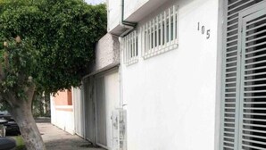 A narrow alleyway with a tree on the left, a building with a garage door on the right, and a number '105' on the wall. - Apartaestudio#4 Itesm Pequeño, Acogedor & Céntrico (Santiago de Querétaro)