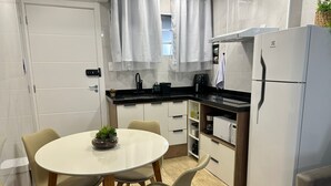 Una cocina moderna con armarios blancos, encimera negra y un refrigerador blanco. Hay una mesa de comedor con cuatro sillas y una planta pequeña encima.