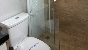 Un baño moderno con ducha envuelta en vidrio, inodoro blanco y panel de pared de madera.
