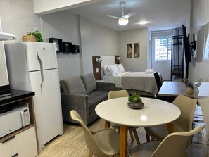 A compact hotel room with a kitchenette, a sofa, a bed, a dining table, and a TV.