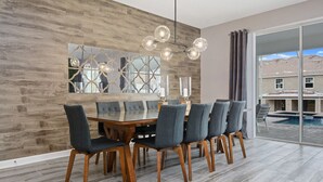 A dining area with a wooden table and chairs, a chandelier, and a large window with a view of a swimming pool and houses. - Last Minute Disney! Private Pool, Hot Tub, Game Room & Themed Bedrooms. Book Now! #21214 (Orlando)