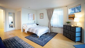 A bedroom with a bed, a dresser, a nightstand, a mirror, and a window with curtains. - PDX Penthouse with Mountain & River Views (Portland)