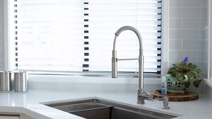 A modern kitchen with a stainless steel sink, a curved faucet, and a window with blinds. - PDX Penthouse with Mountain & River Views (Portland)