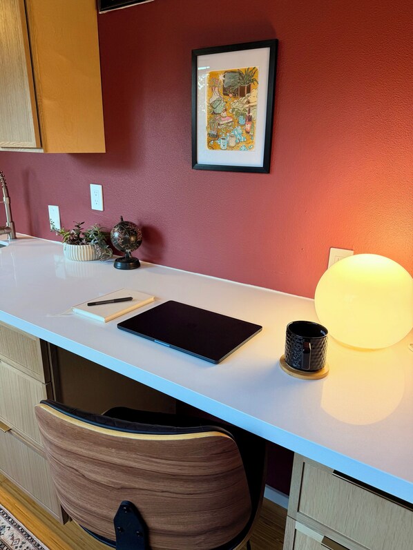 A modern workspace with a white desk, a tablet, a mug, a globe, and a framed artwork on the wall.