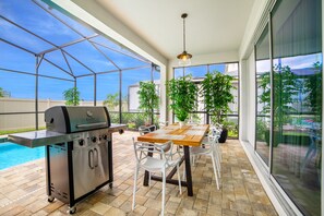 Eine Terrassengruppe im Freien mit Grill, Esstisch, Stühlen und Kübelpflanzen.