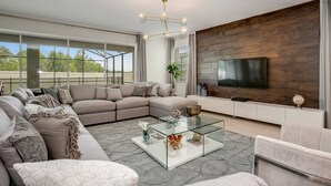 Un salon moderne avec un canapé d’angle, une table basse en verre et un téléviseur à écran plat fixé à un mur en bois.