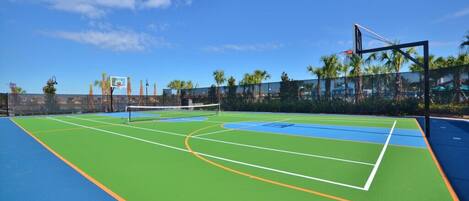 An outdoor tennis court with a net, surrounded by a fence and palm trees.