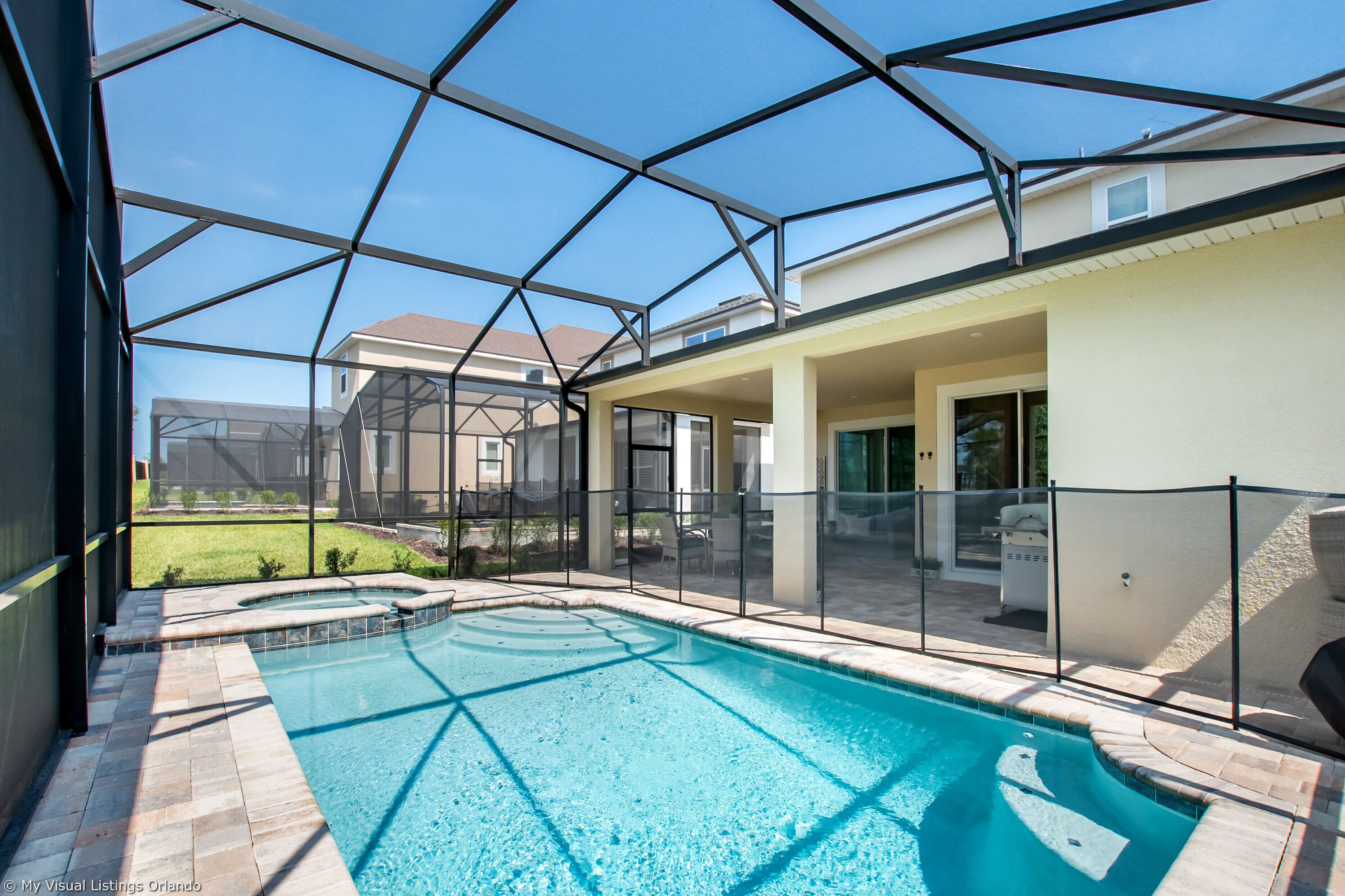 A swimming pool with a glass enclosure, surrounded by a patio area with outdoor furniture.