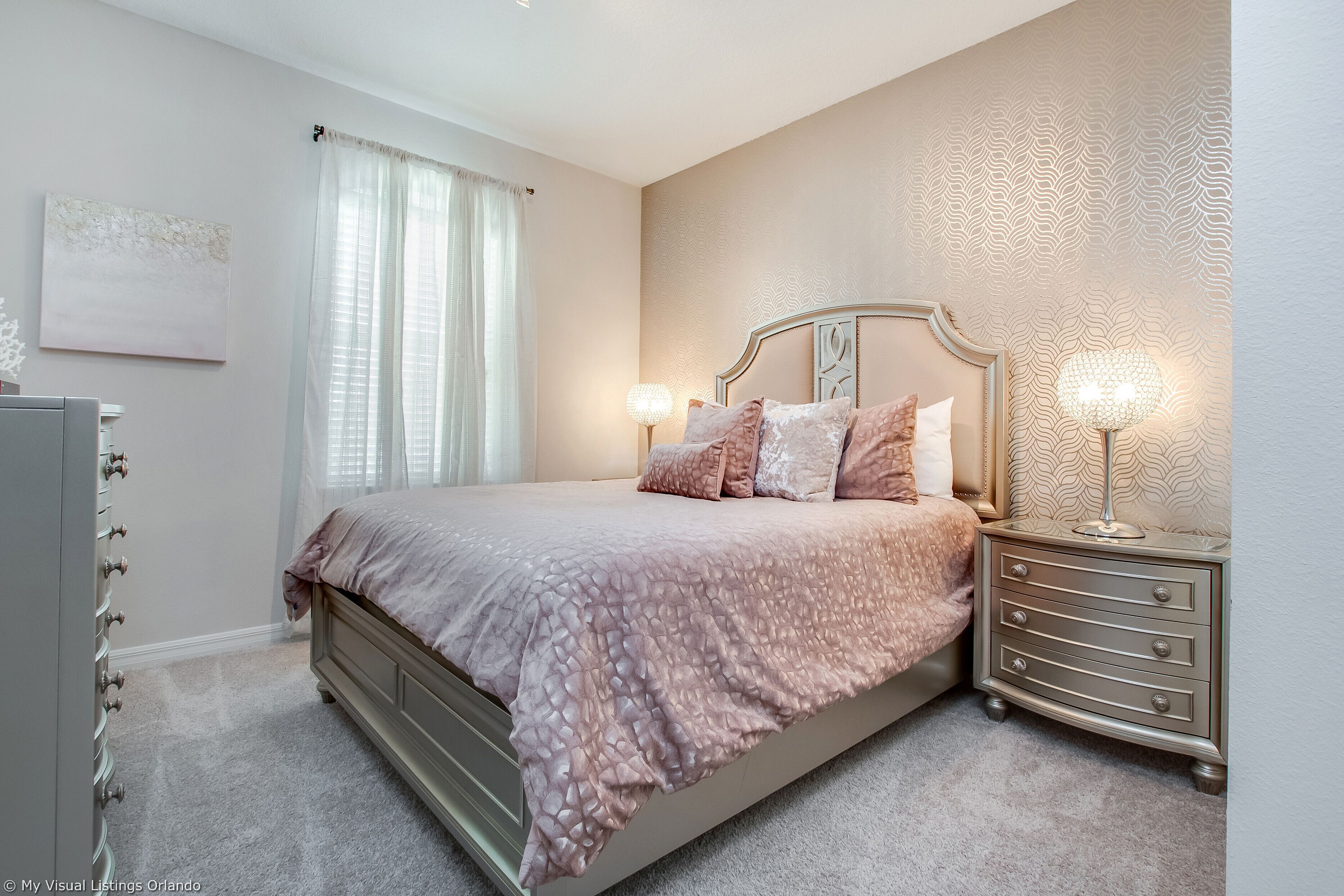 A bedroom with a bed, nightstands, a dresser, and a window with curtains.
