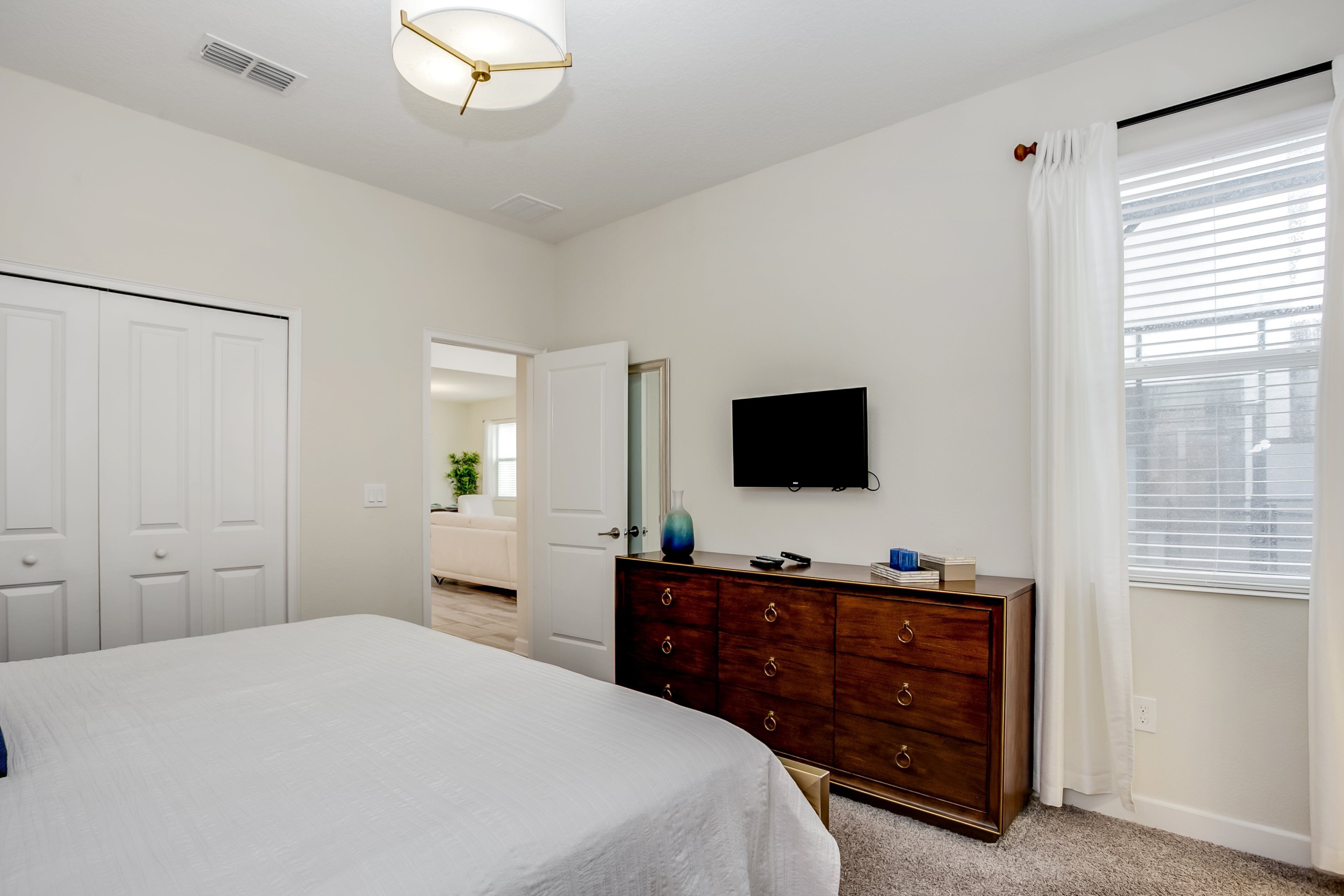 A bedroom with a bed, a dresser, a television, and a window with blinds.