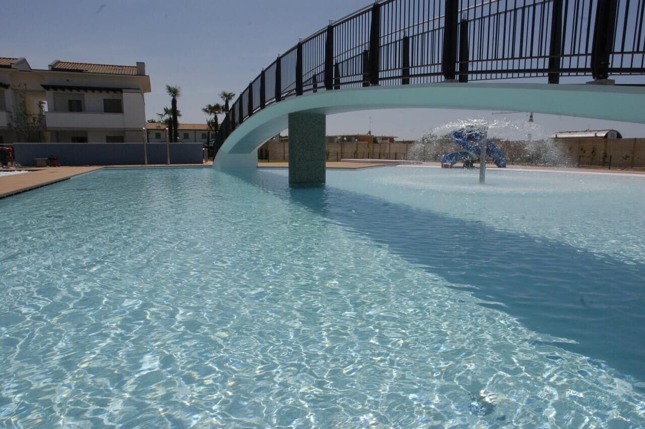 A clear swimming pool with a bridge over it, surrounded by buildings.