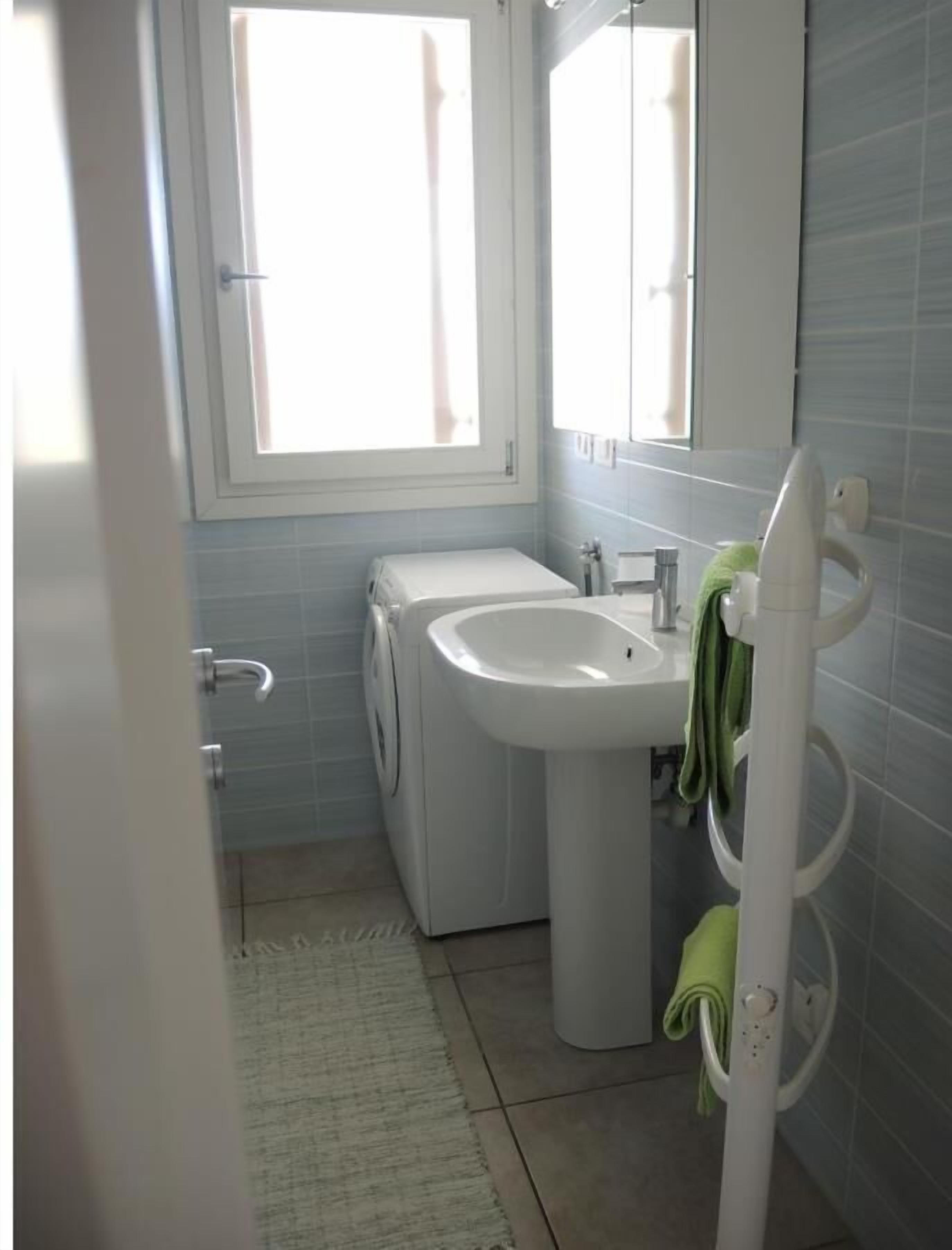 A bathroom with a washing machine, a sink, and a mirror.