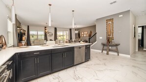 A modern kitchen with a large island, black cabinets, stainless steel appliances, and pendant lighting.