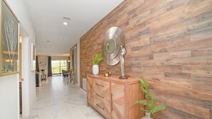 A hallway with a wooden wall, a marble floor, a wooden cabinet with a mirror, and a potted plant.