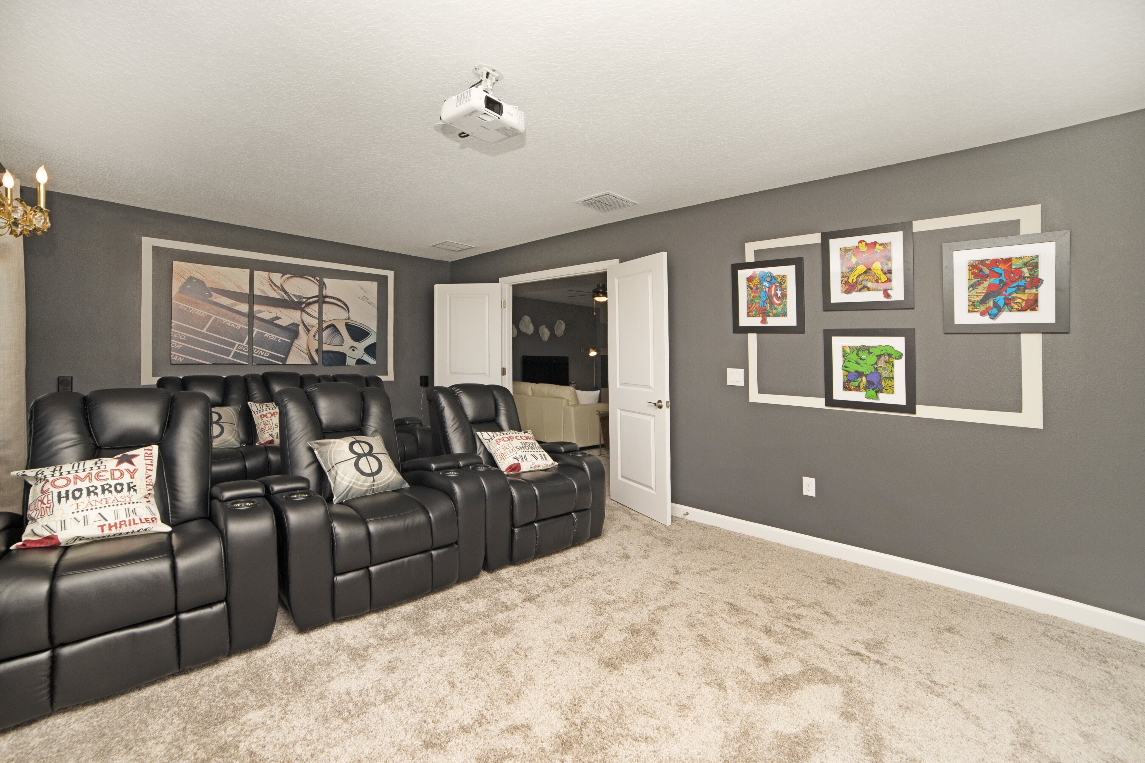 A home theater room with a black leather recliner sofa, a projector ceiling, and framed artwork on the walls.
