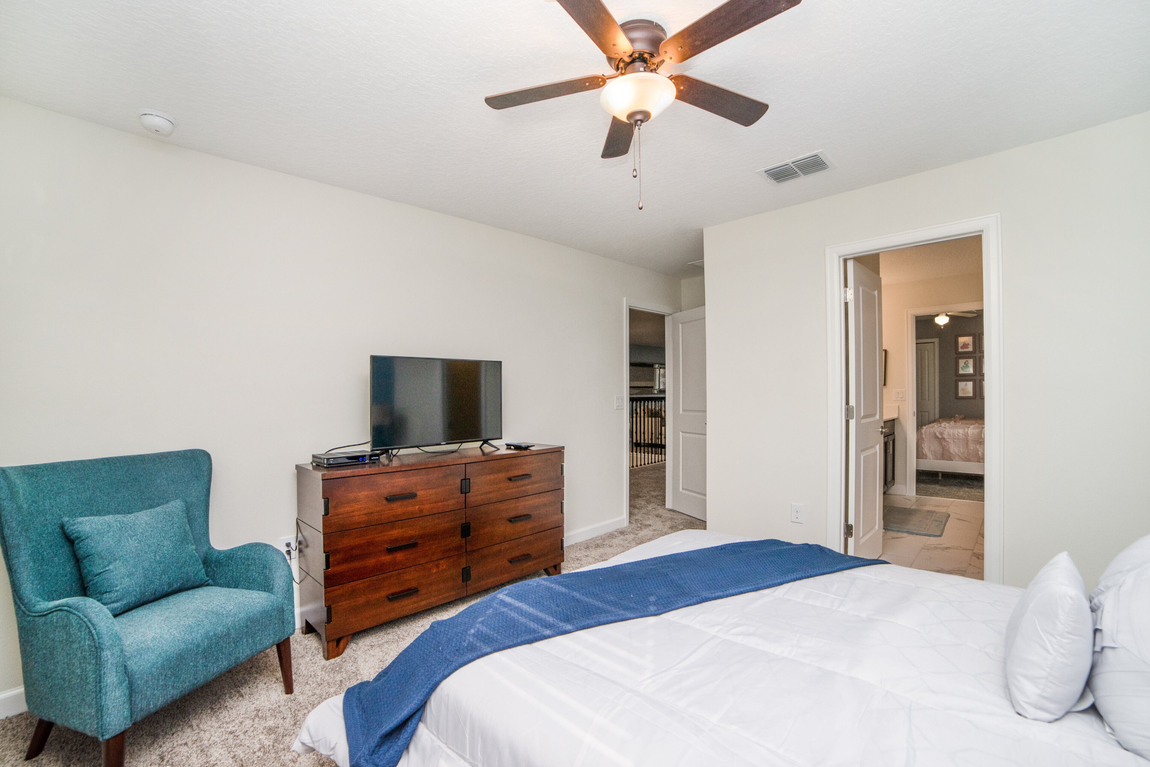 A bedroom with a bed, a dresser, a television, and a ceiling fan.
