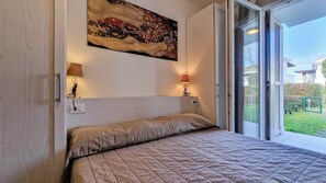 A bedroom with a bed, two bedside lamps, a painting on the wall, and a sliding glass door leading to a balcony. - Residenz Evanike Wohnung B2 1S Erdgeschoss M2 für 4 Personen (Bibione)