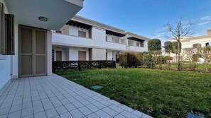 A modern residential building with a tiled patio, a well-maintained lawn, and a small water feature. - Residenz Evanike Wohnung B2 1S Erdgeschoss M2 für 4 Personen (Bibione)