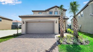 A residential house with a garage, paved driveway, and palm trees.