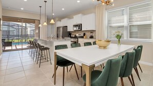 A modern kitchen with white cabinets, a large island, and a dining area with green chairs.