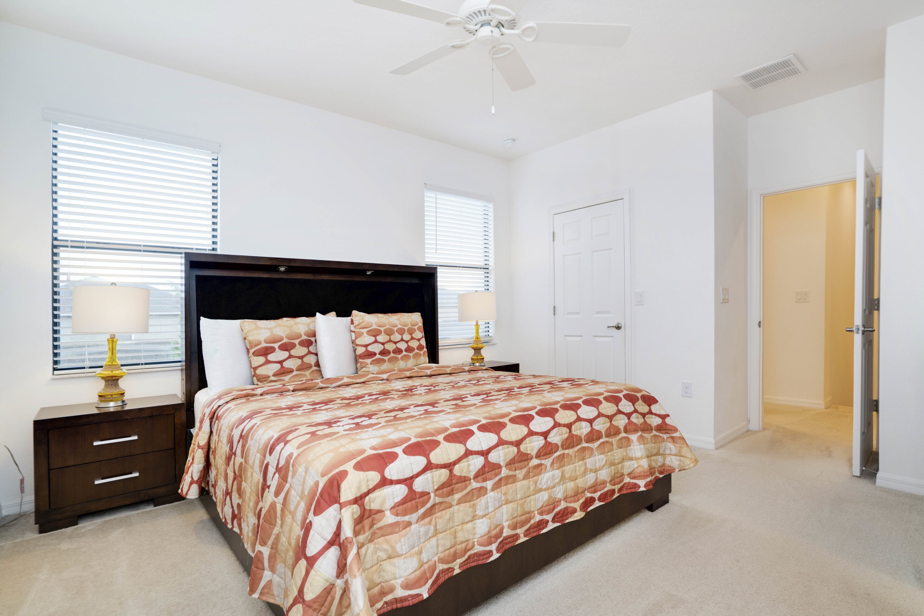 A bedroom with a bed, nightstands, a ceiling fan, and a door.