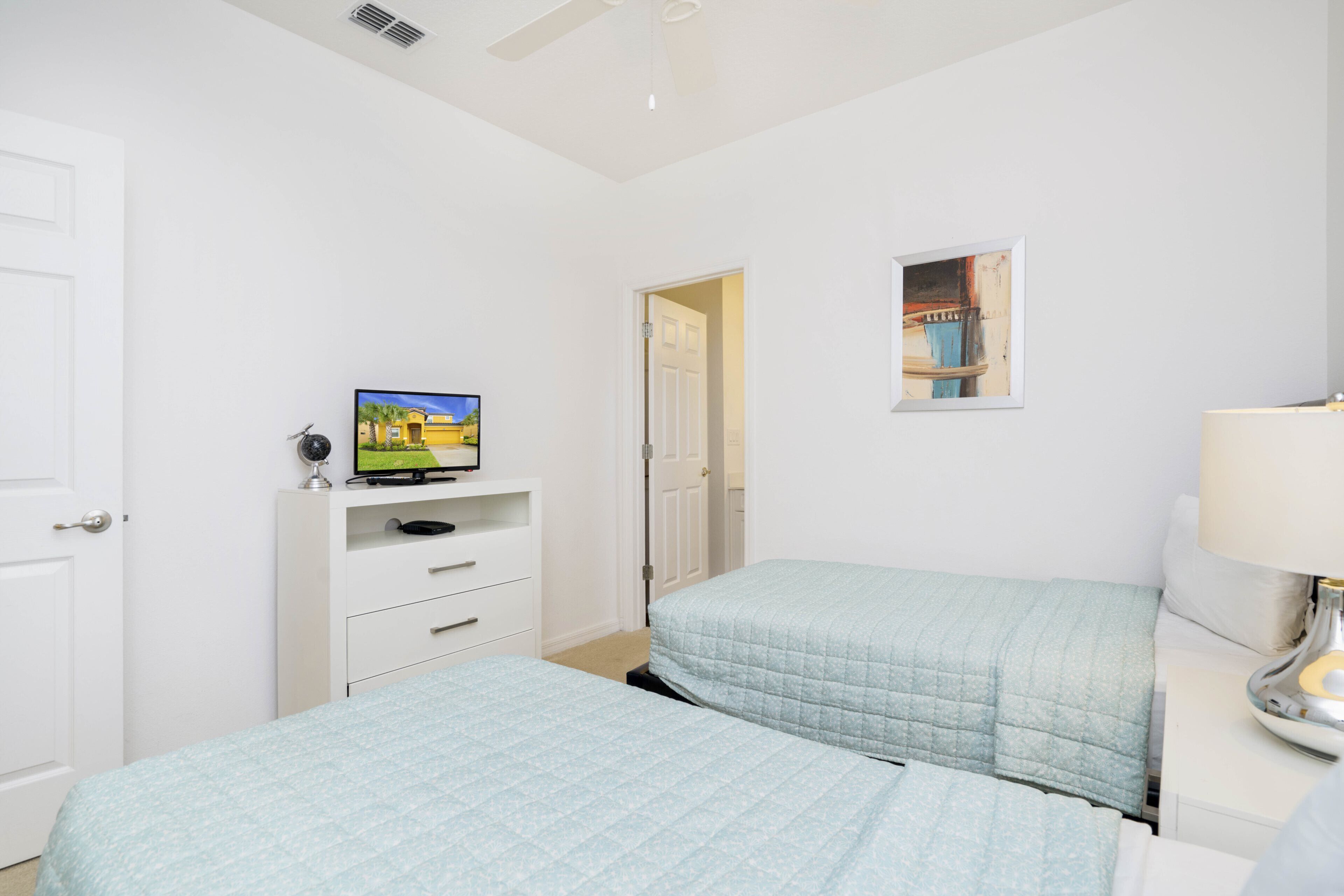 A bedroom with two beds, a TV on a dresser, a door, and a small picture on the wall.
