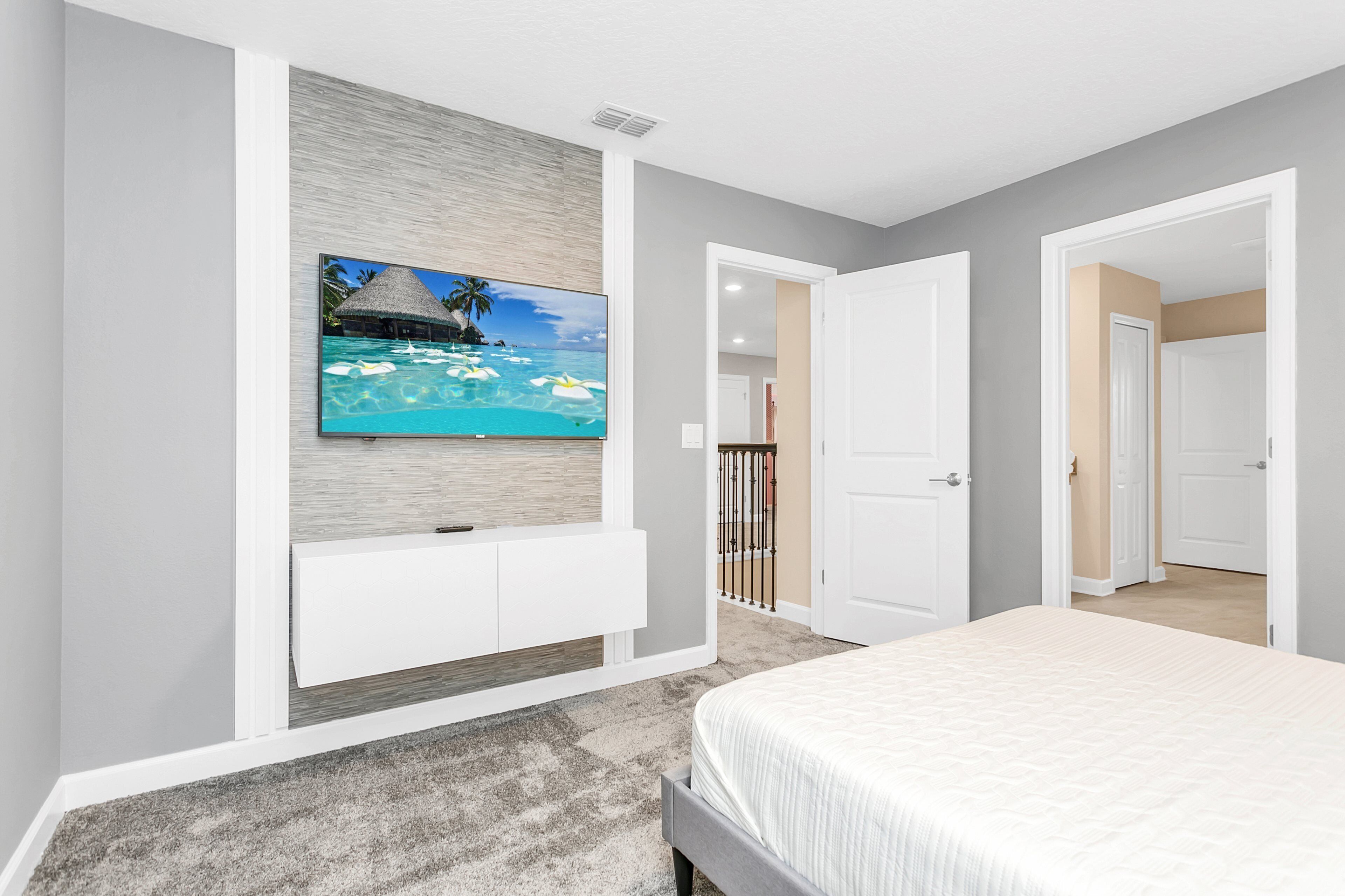 A bedroom with a bed, a TV mounted on the wall, and a door leading to another room.