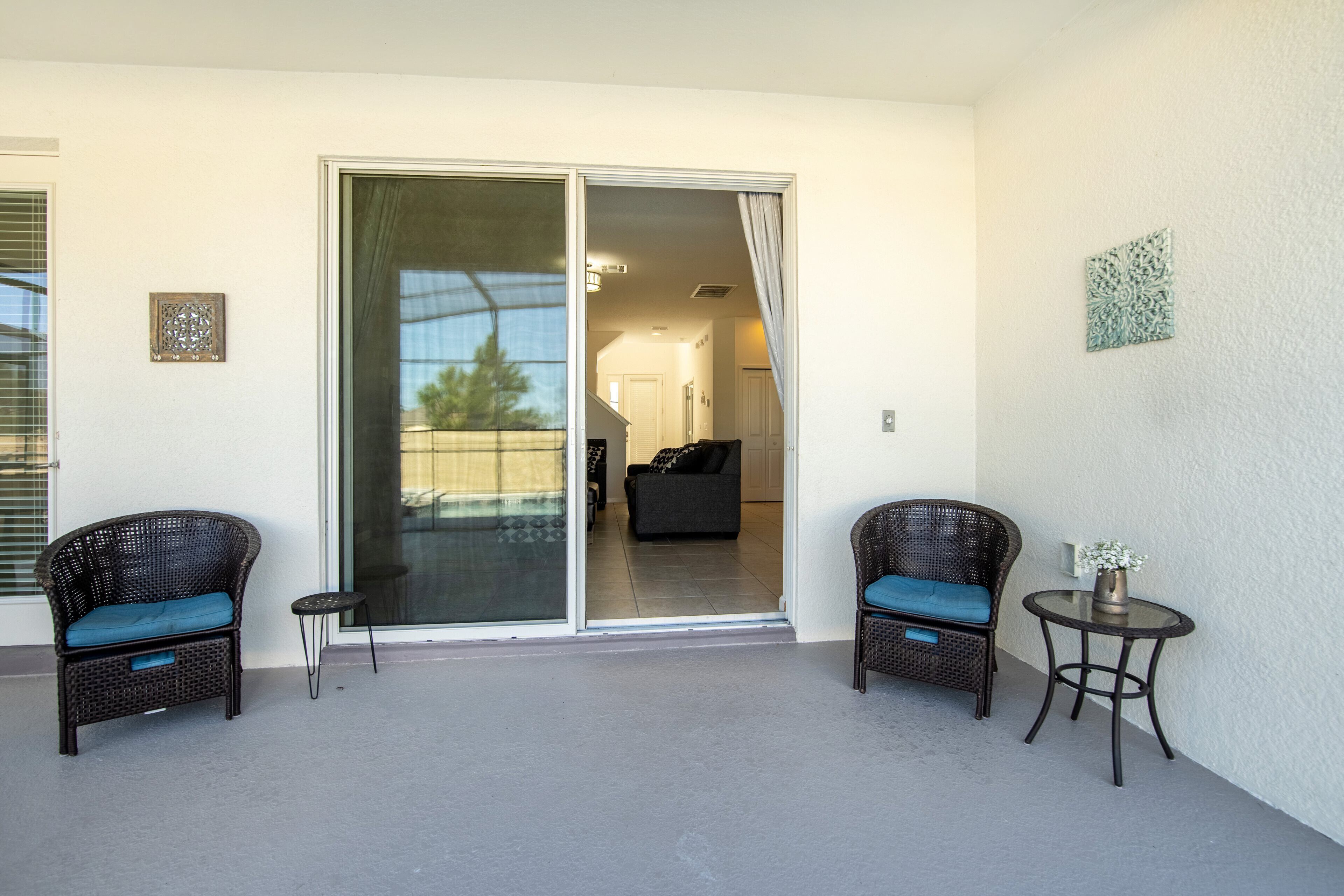 A balcony with two wicker chairs, a small round table, and a sliding glass door leading to an interior space.