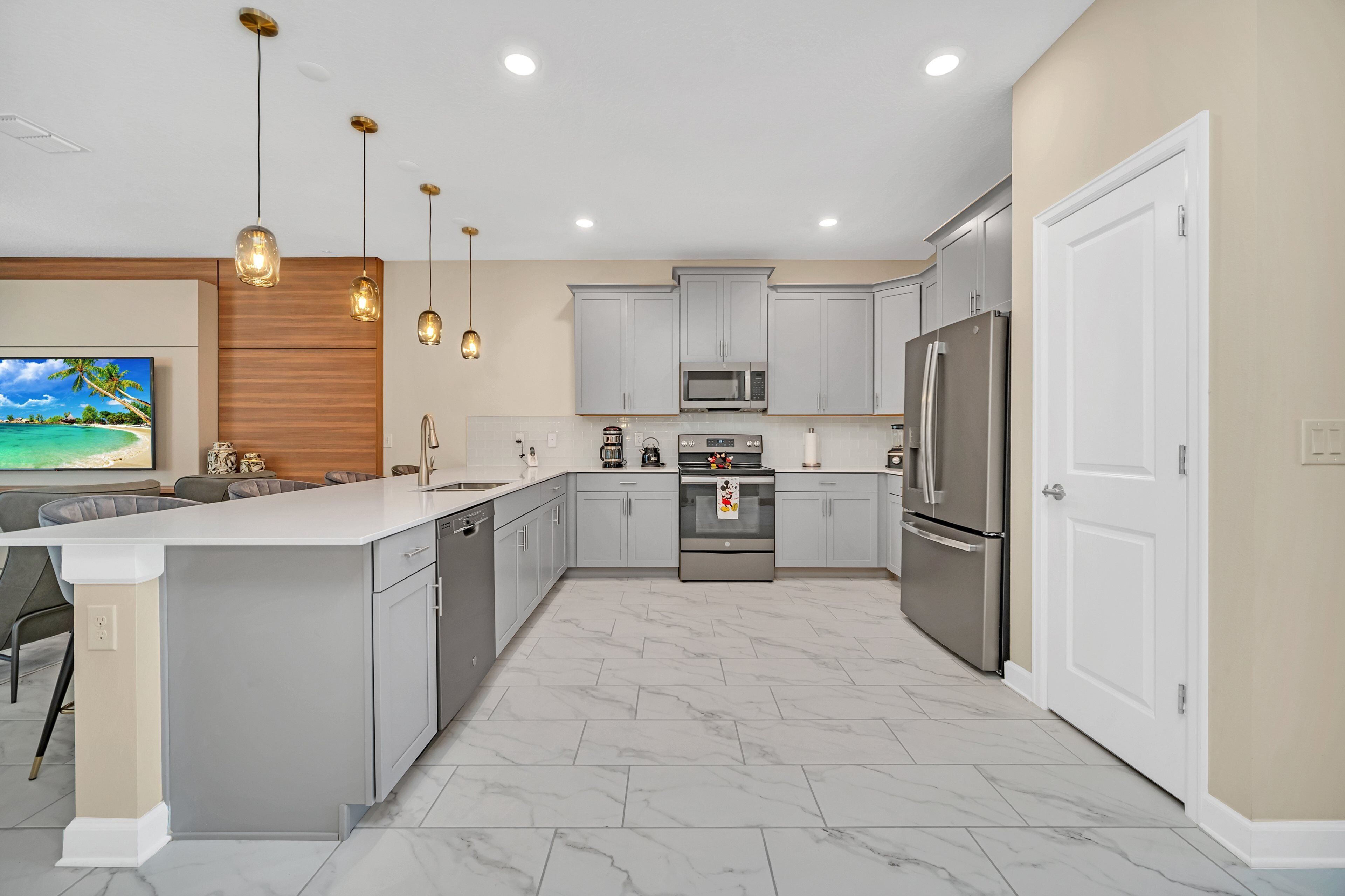 A modern kitchen with grey cabinets, stainless steel appliances, and a marble floor.