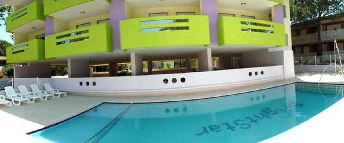 Un hotel moderno con zona de piscina, varios balcones y una piscina azul cristalina.
