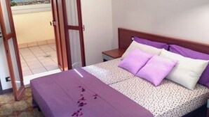 Une chambre à coucher avec un lit, une table de chevet et une vue sur la mer, visible à travers une porte ouverte.