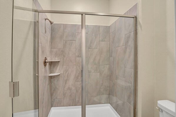 A modern bathroom with a glass-enclosed shower, beige tiles, and a white toilet.
