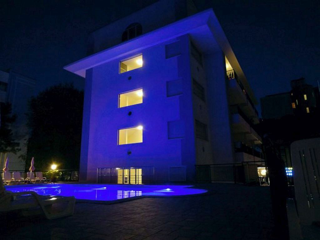 Ein modernes Gebäude mit Poolanlage bei Nacht, beleuchtet mit blauem Licht.