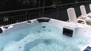 A hot tub with clear water, surrounded by white lounge chairs.